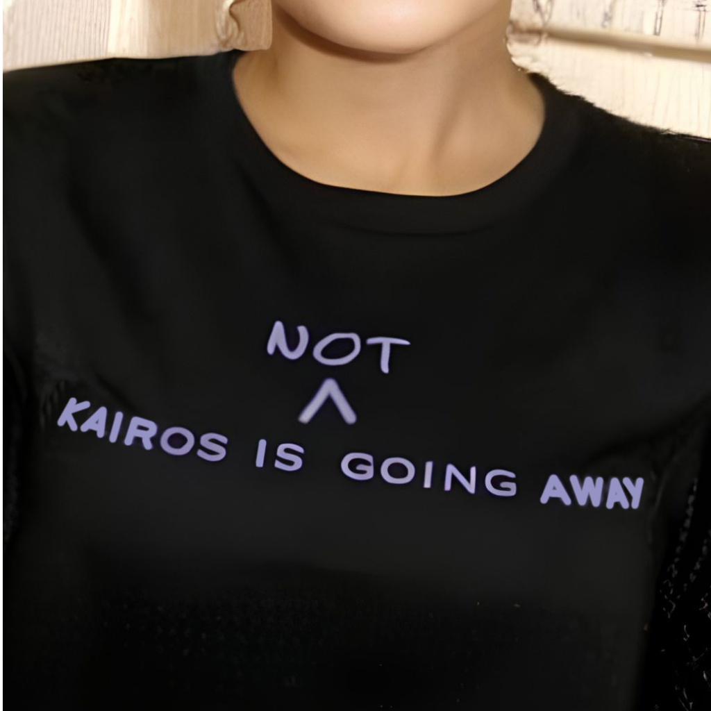 Black T-shirt reading ‘KAIROS is not going away’ with the word ‘not’ handwritten above